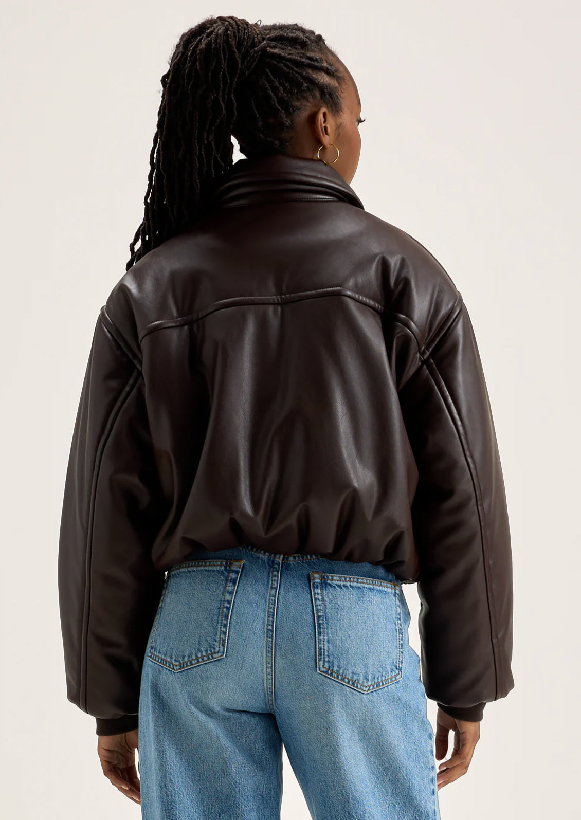 A woman wearing a bomber style jacket in brown faux leather.