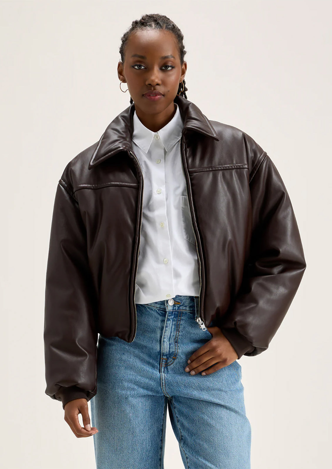 A woman wearing a bomber style jacket in brown faux leather.