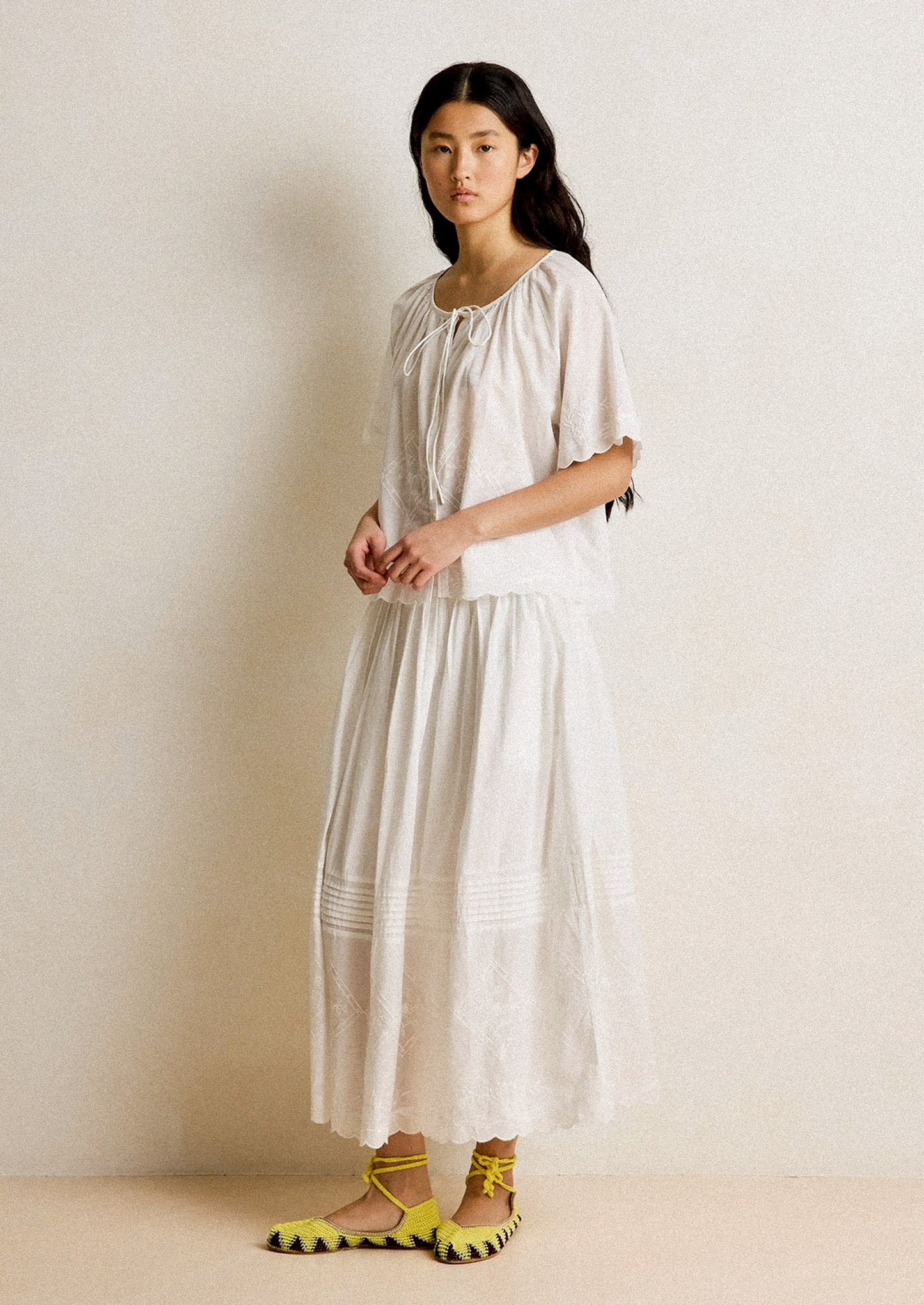 Woman wearing a white dress with yellow shoes against a plain background