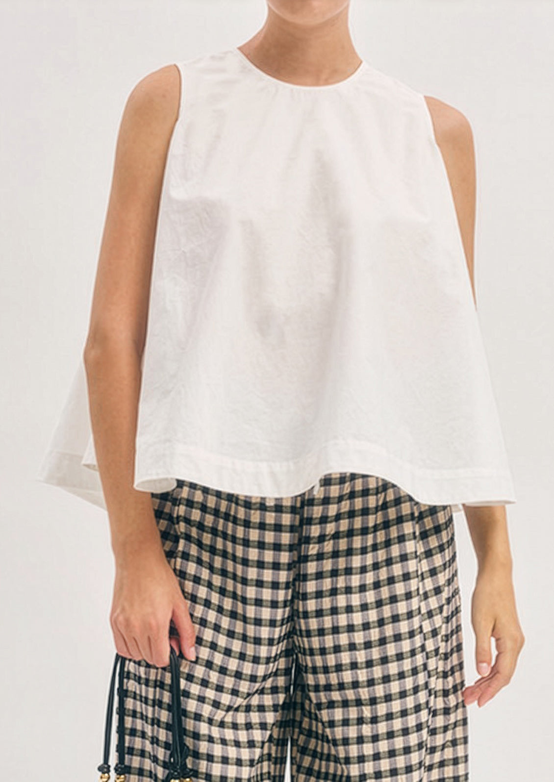 Person wearing a white sleeveless top and plaid pants on a plain background