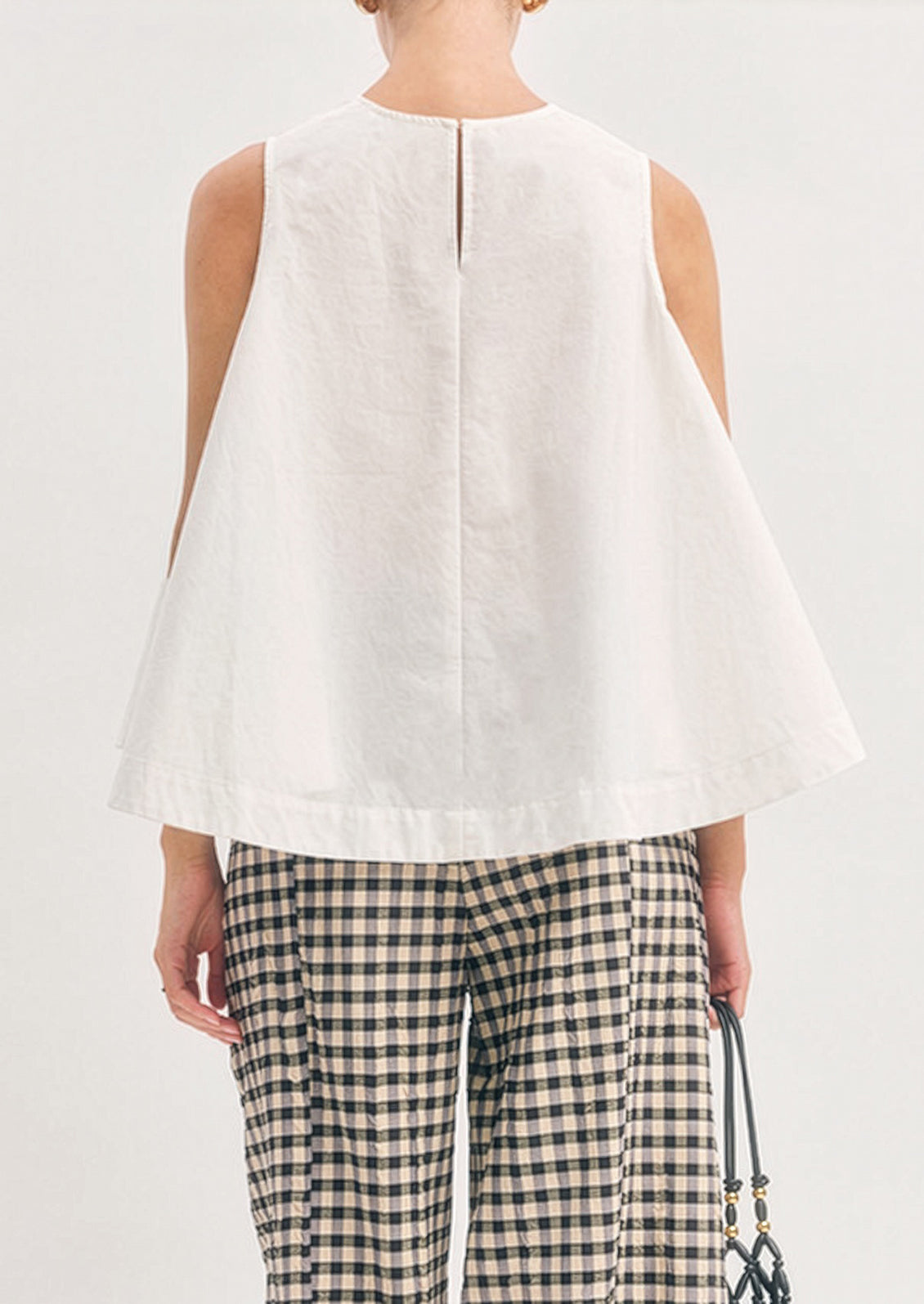 Person wearing a white sleeveless top and plaid pants on a plain background