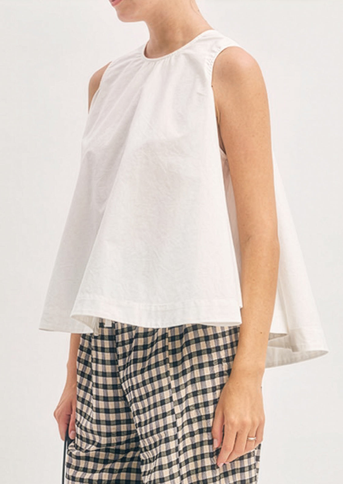 Person wearing a white sleeveless top and plaid pants on a plain background