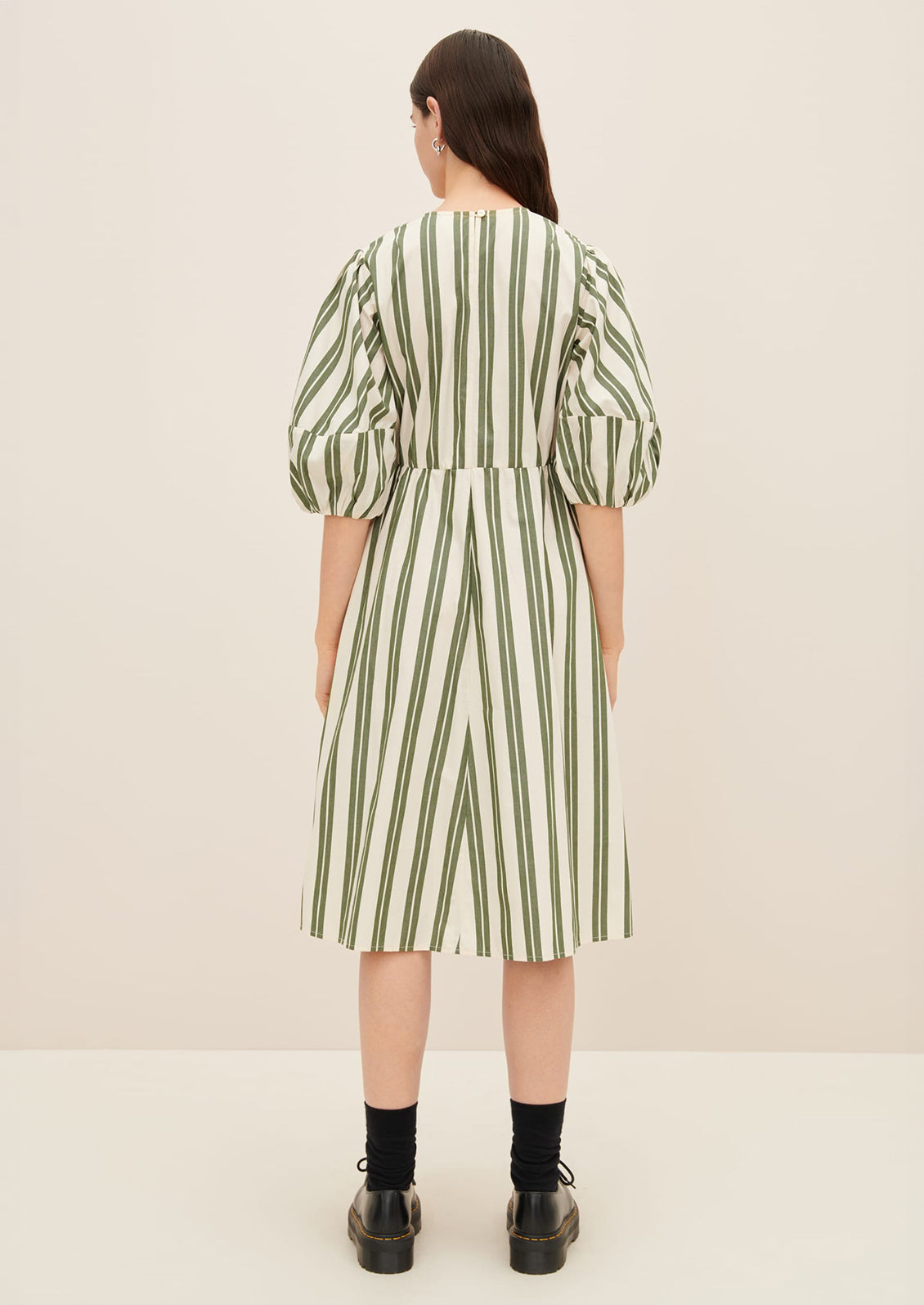 A woman wearing a cream dress with double wide vertical striping in forest green.