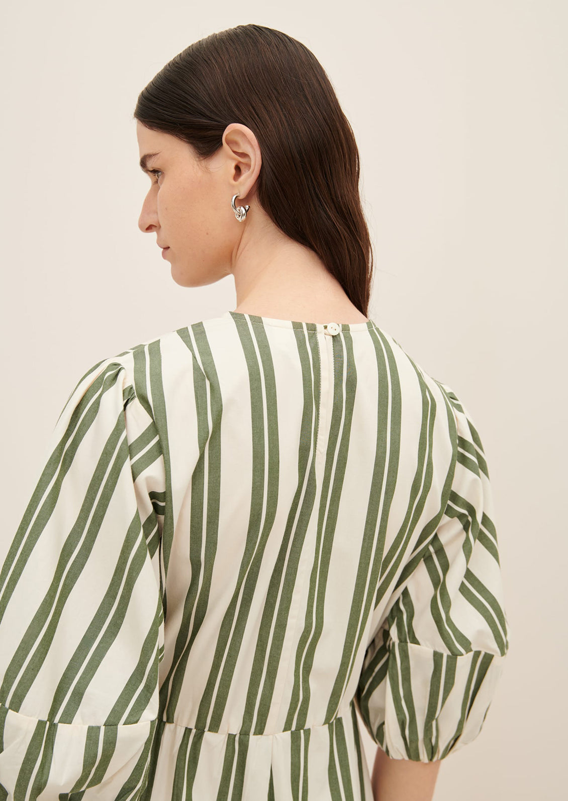 A woman wearing a cream dress with double wide vertical striping in forest green.