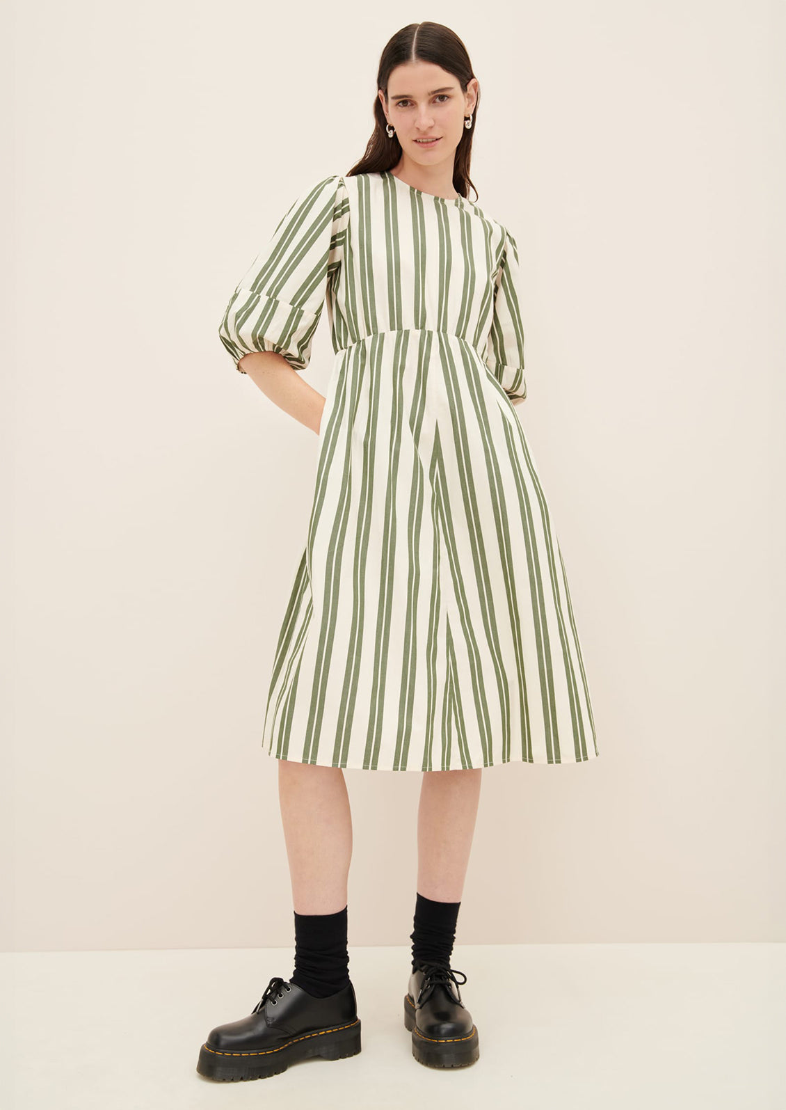 A woman wearing a cream dress with double wide vertical striping in forest green.