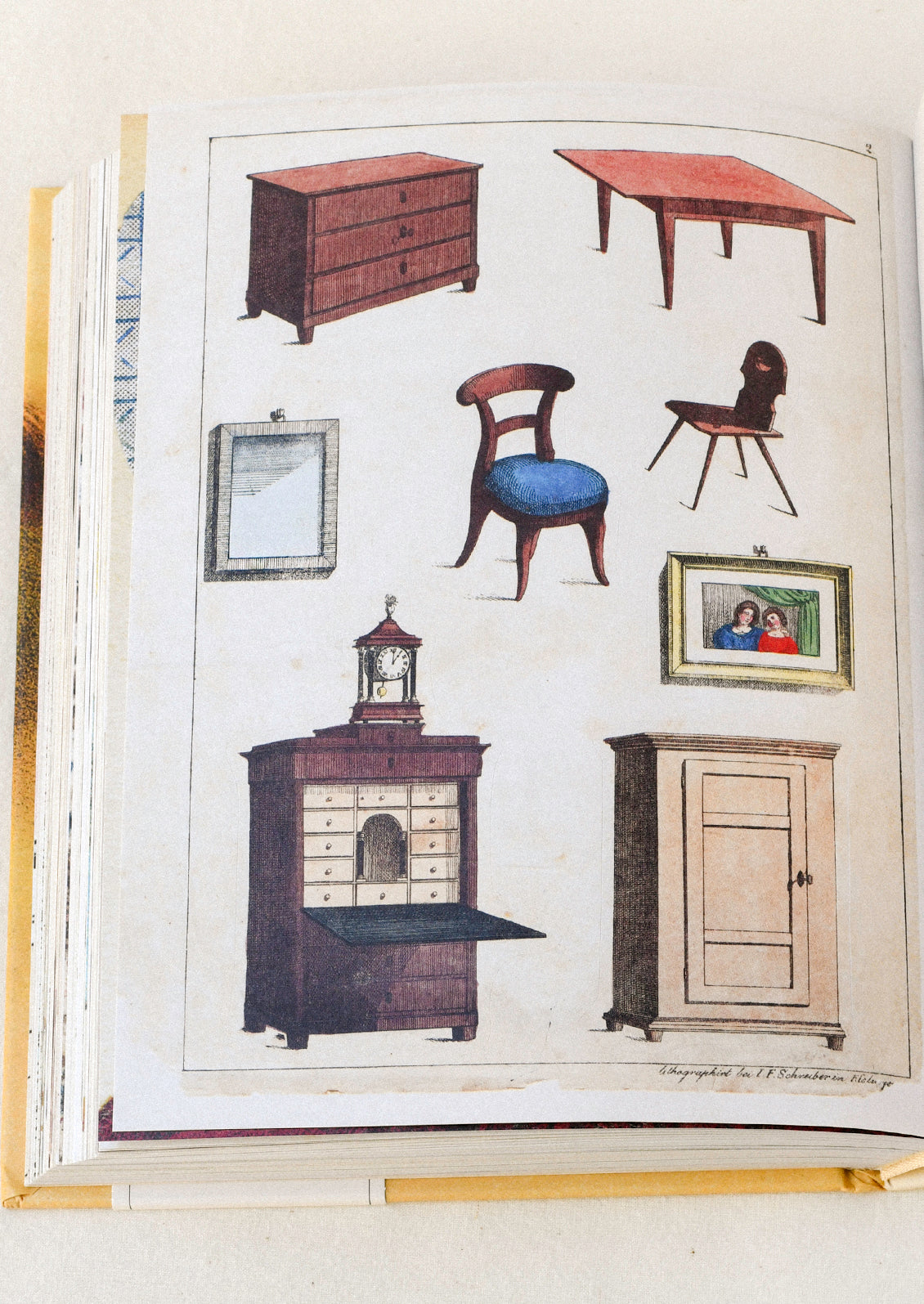 A sticker book sitting open on a table featuring illustrations of various pieces of furniture and picture frames.