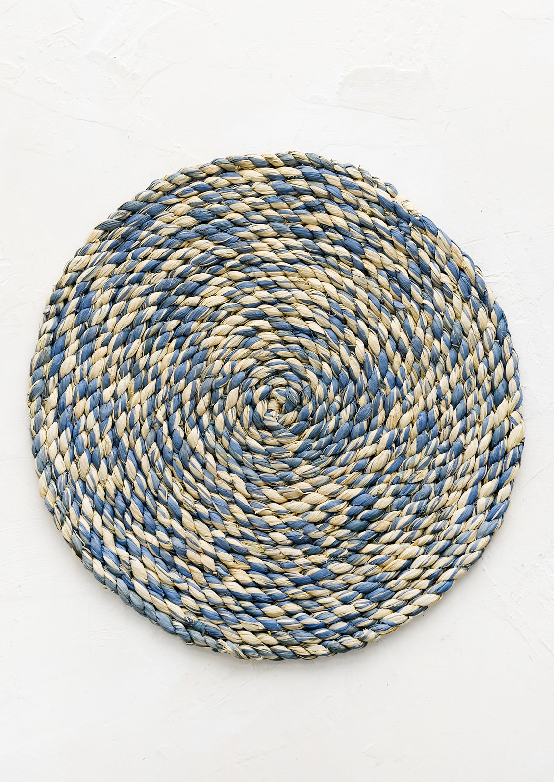 A round woven raffia placemat in natural and mirage blue.