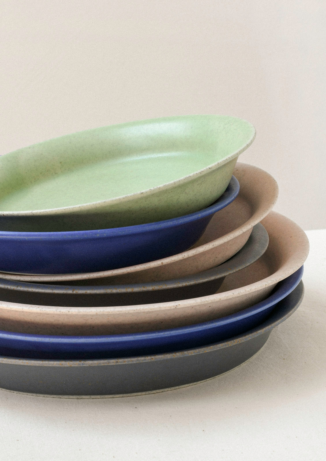 A stack of small and large green, blue, pink, and gray ceramic plates sitting on a table against a cream colored wall.