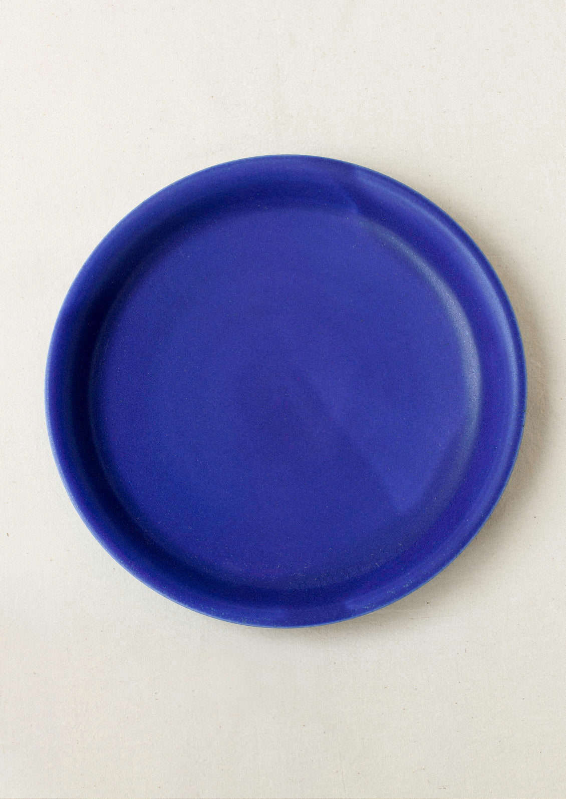 A large ceramic dinner plate in cobalt blue on a cream background.