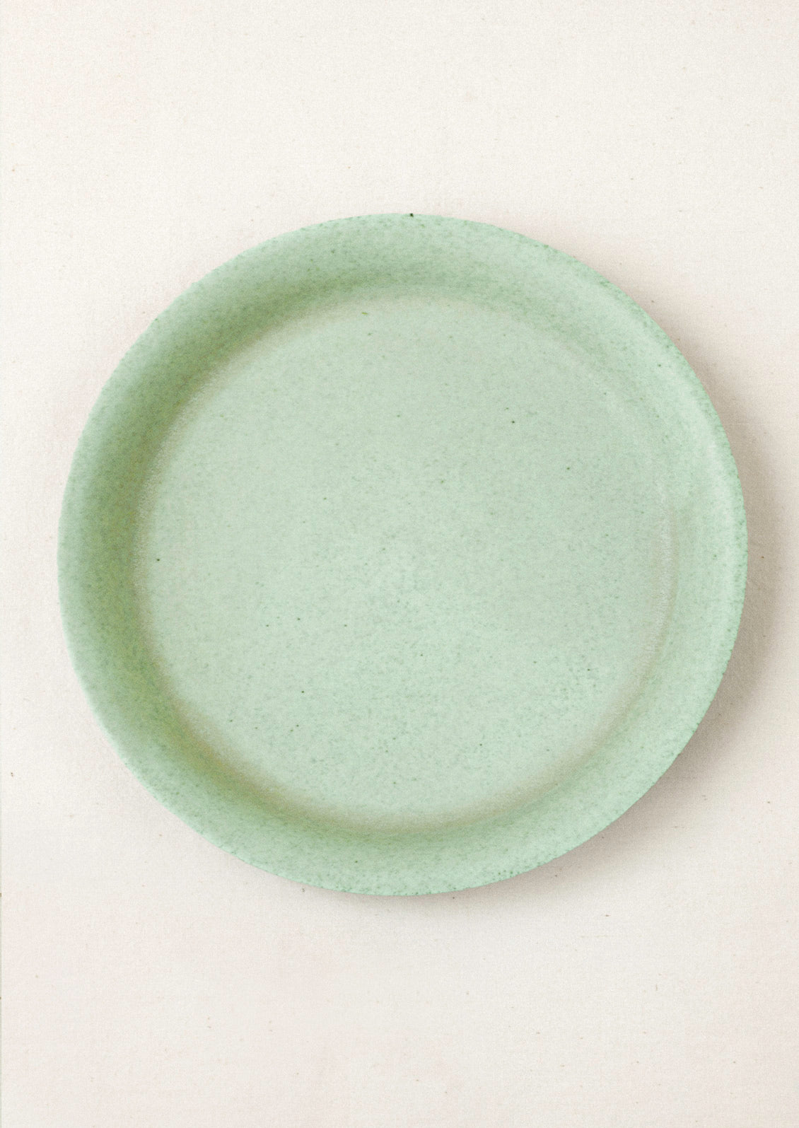 A large ceramic dinner plate in a green color on a cream background.