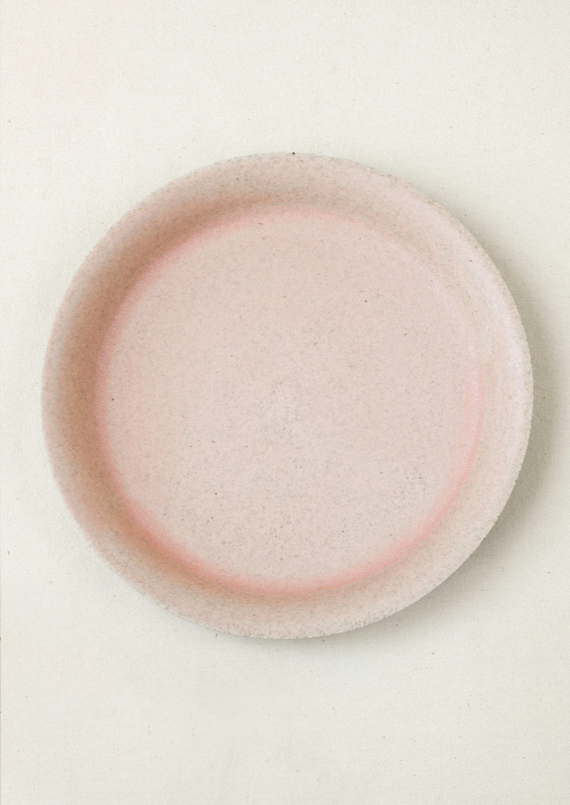 A large ceramic dinner plate in a light pink color on a cream background.