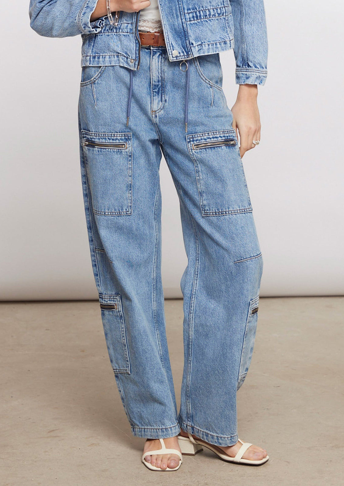 A person wearing light wash jeans with zip details on pockets.