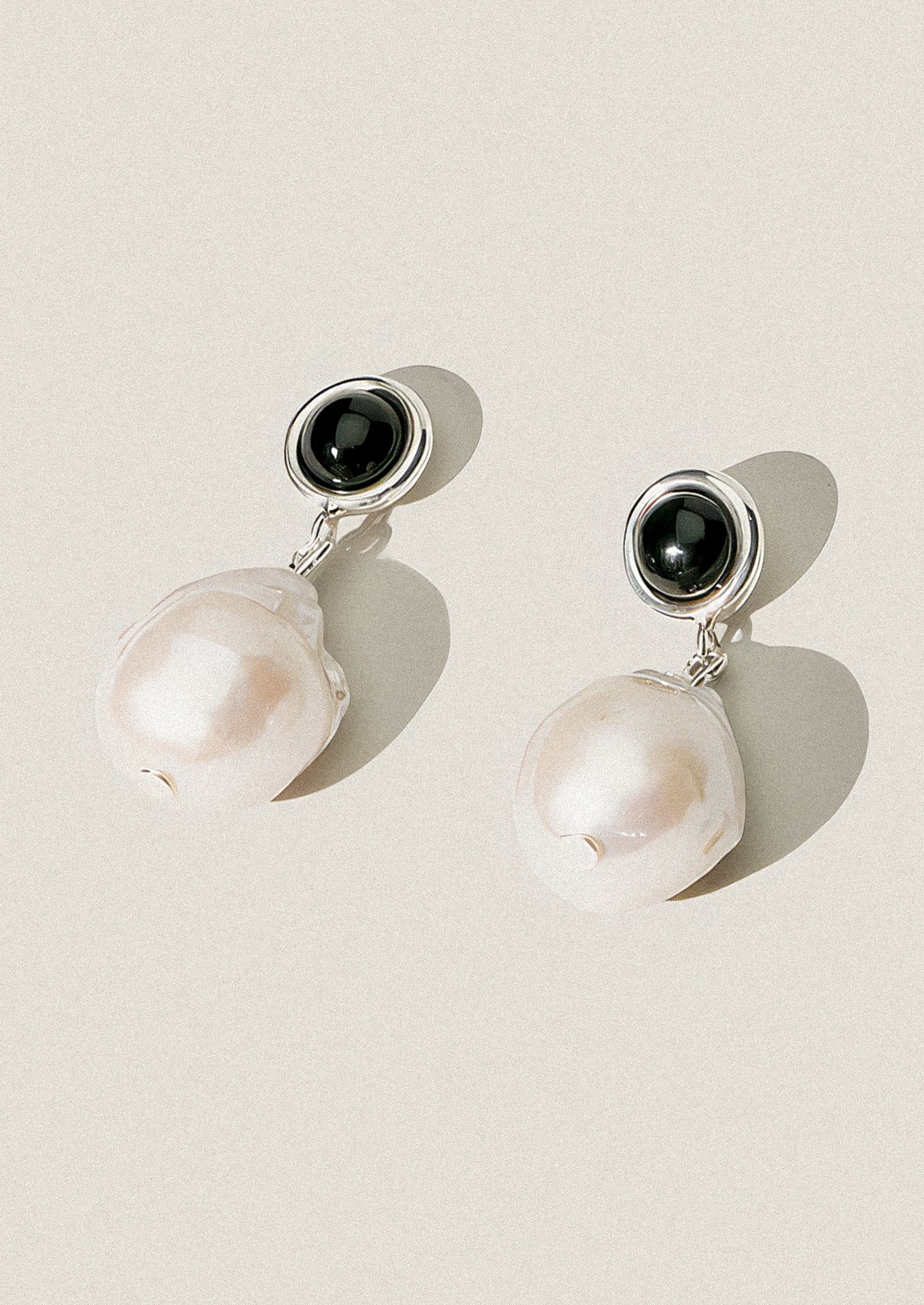Pair of earrings with black stones and pearl beads on a light background