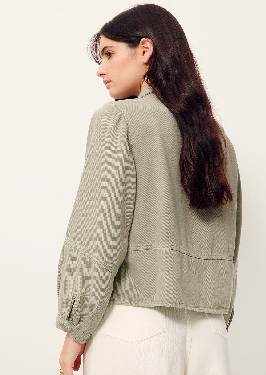Woman wearing light gray denim shirt jacket, seen from behind. 