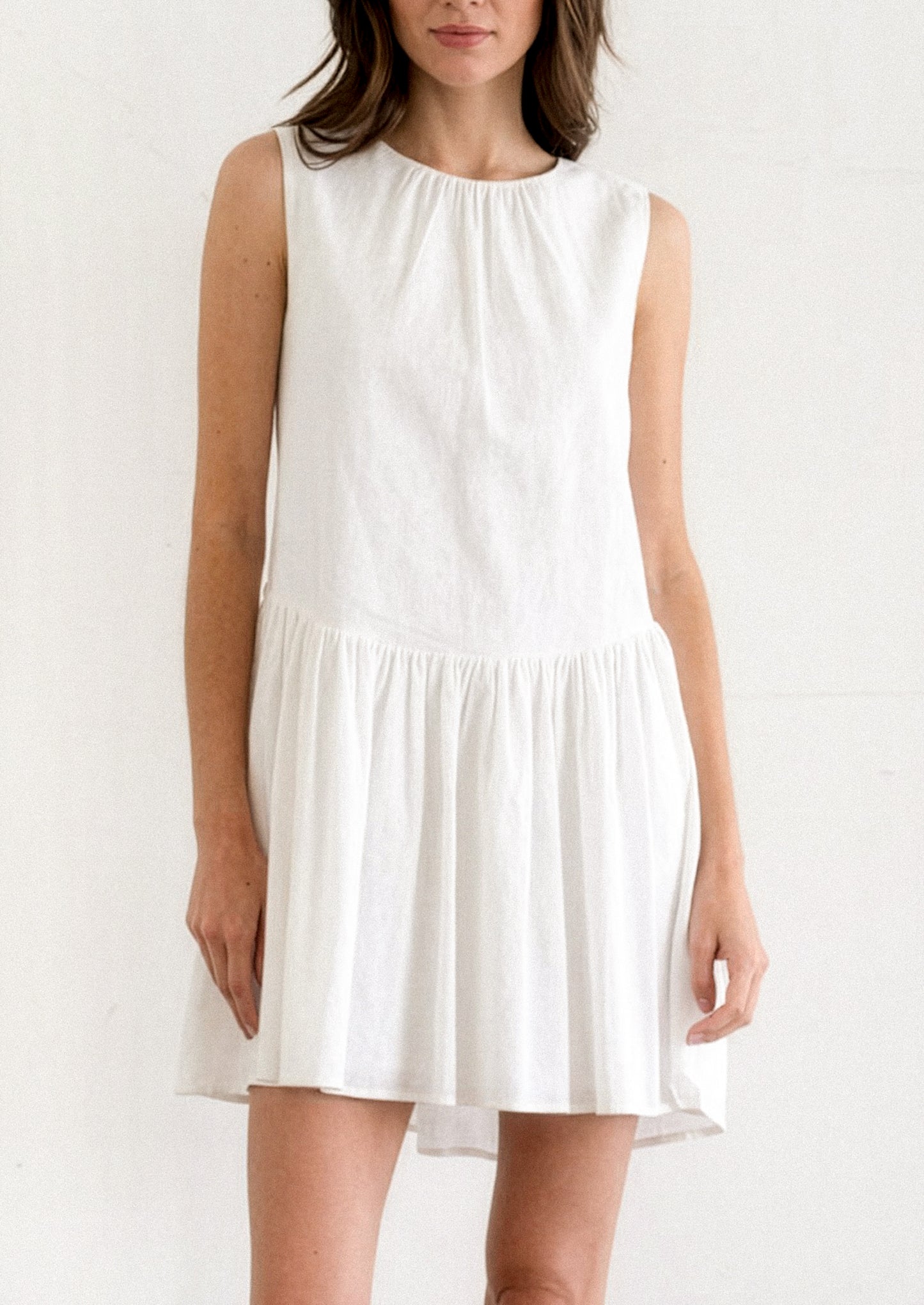 A person wearing a white mini dress with dropwaist and tieback detail.