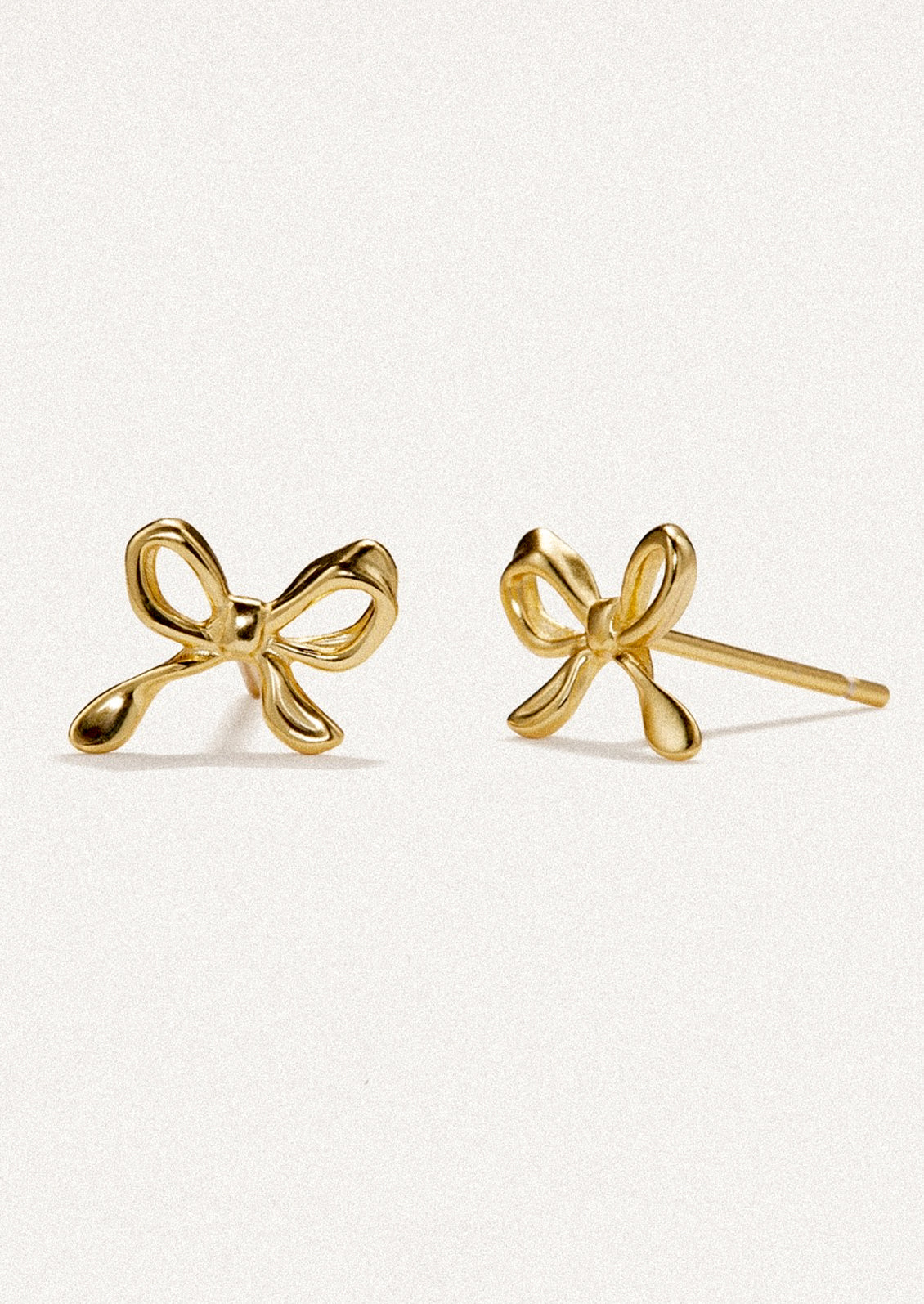 A pair of small stud earrings in gold, in the shape of a small bow.