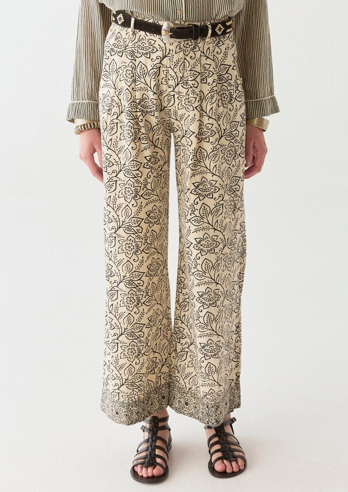 A woman wearing a pair of cream pants with black floral print.