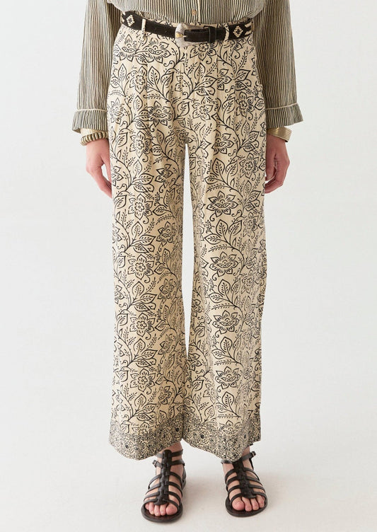 A woman wearing a pair of cream pants with black floral print.