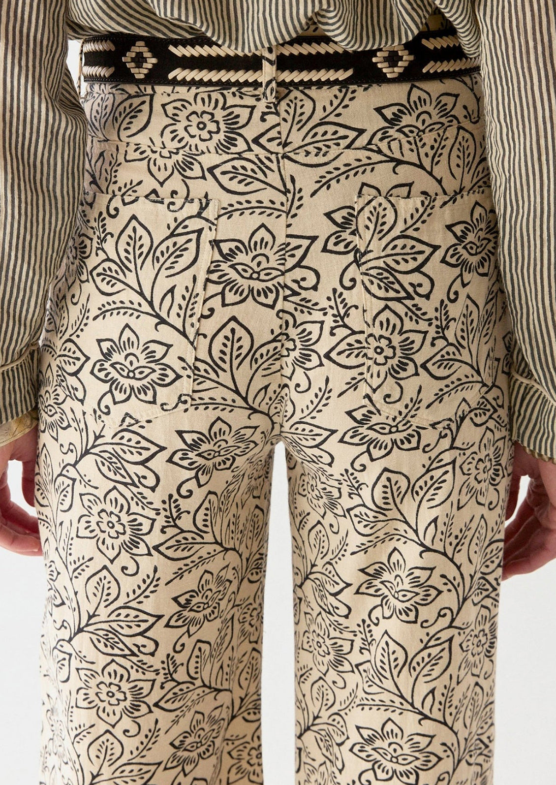 A woman wearing a pair of cream pants with black floral print.