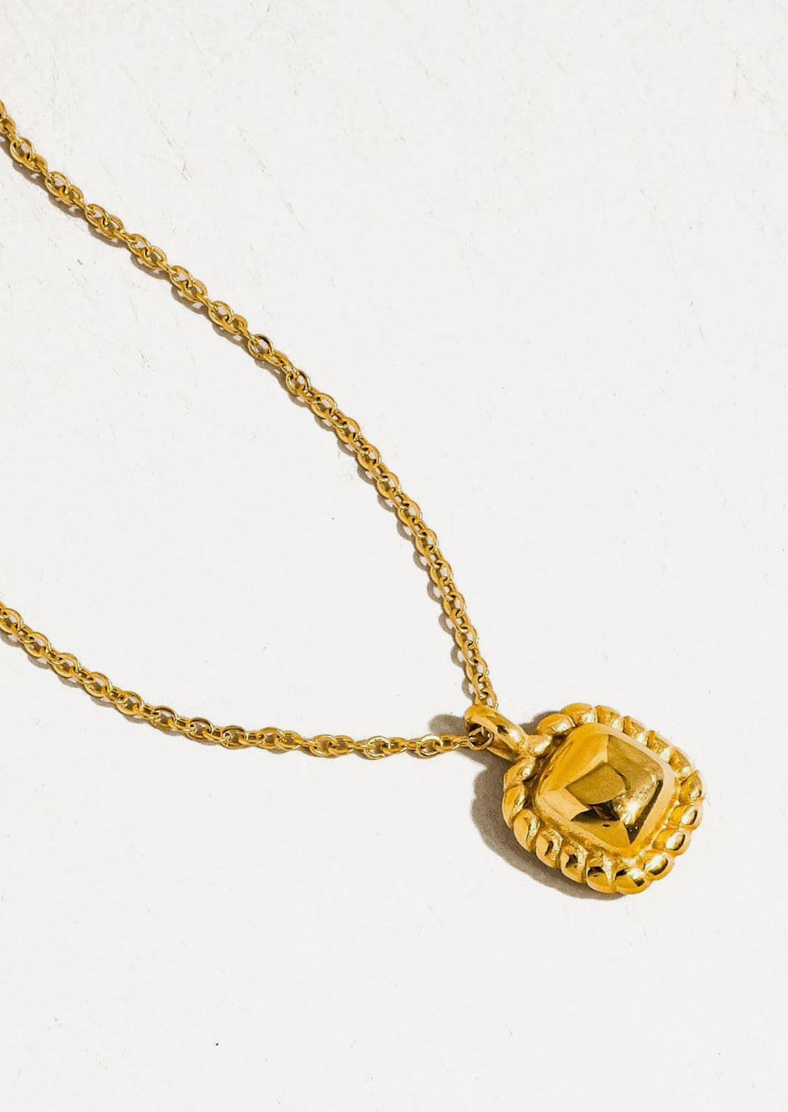 A gold necklace with square vintage style charm.