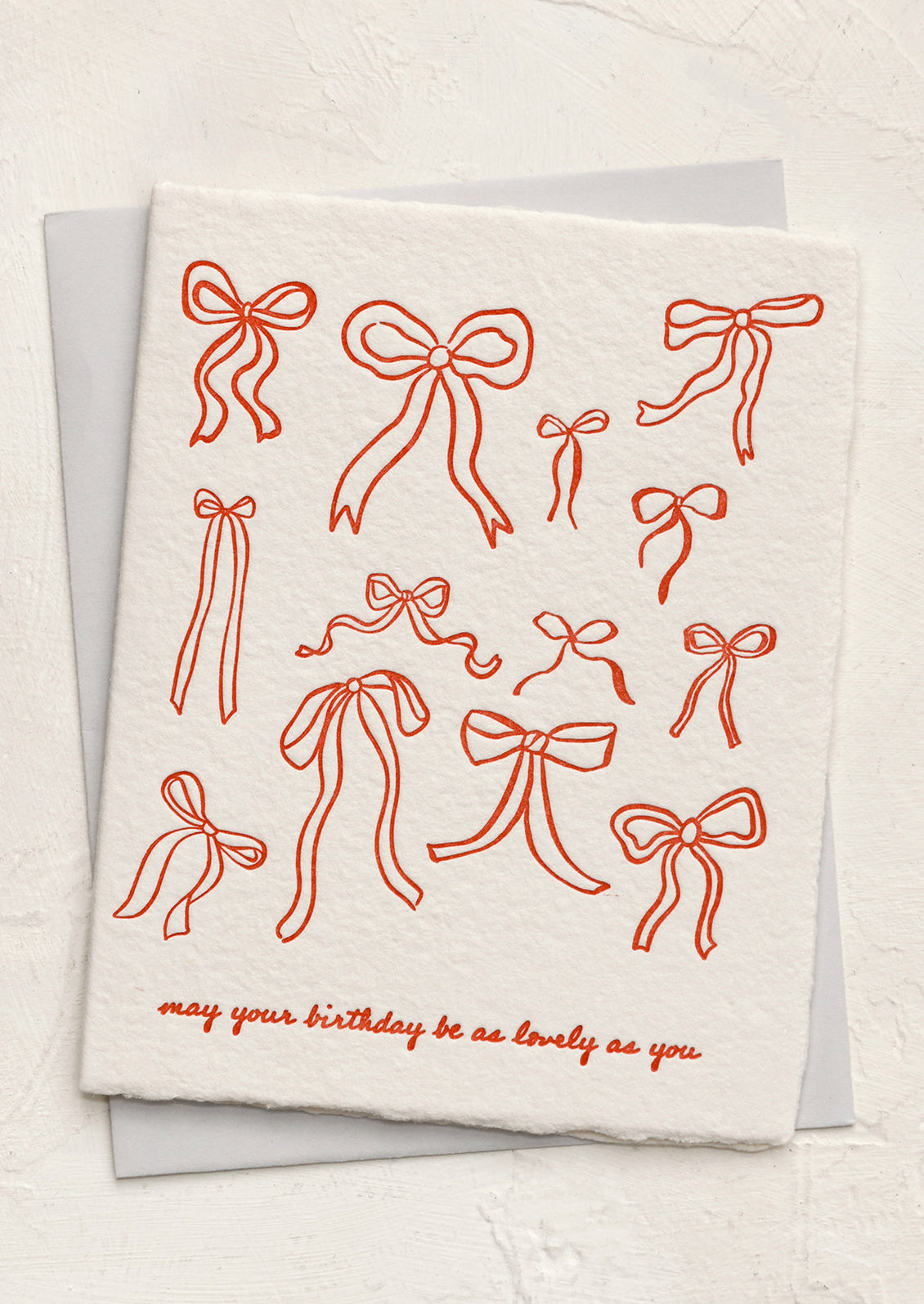 A greeting card with allover red bow print, text reads "May your birthday be as lovely as you".