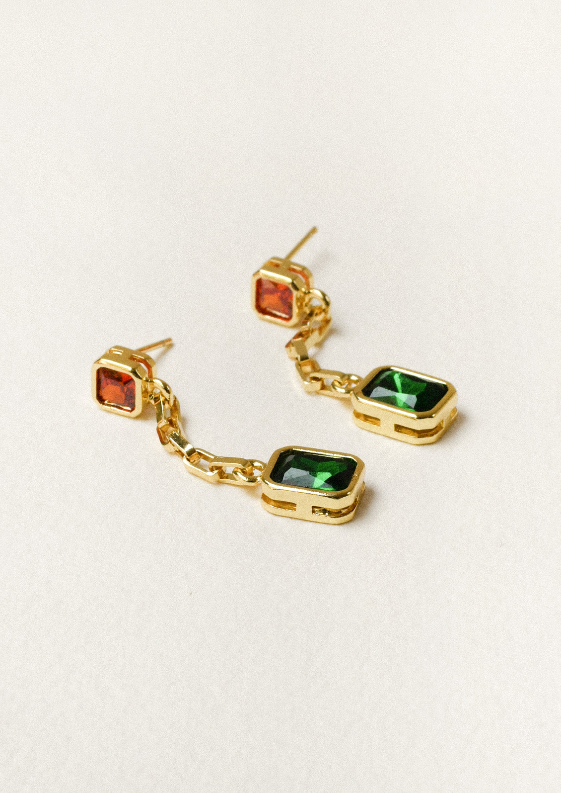 A pair of gold chain dangling earrings with orange and green gems on a white background.