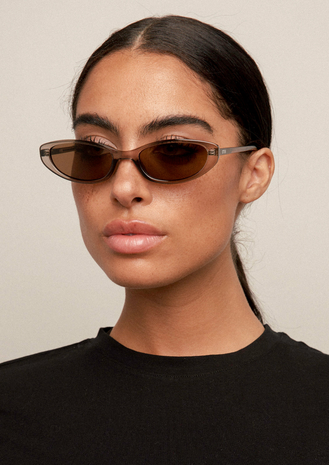 A woman wearing a pair of cat eye sunglasses with a transparent olive frame and brown lenses.