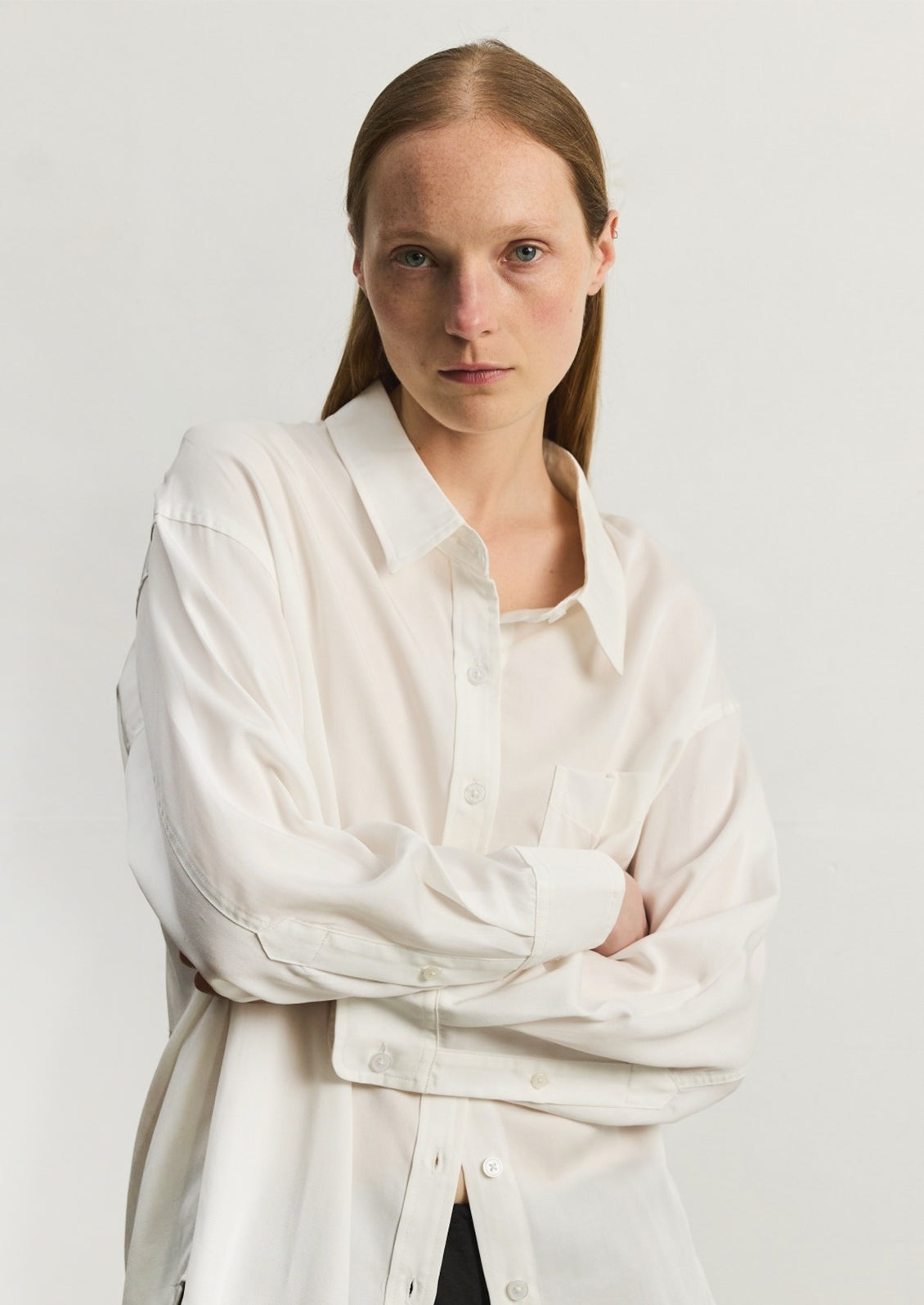 A woman wearing a relaxed, fluid fabric white button front shirt.