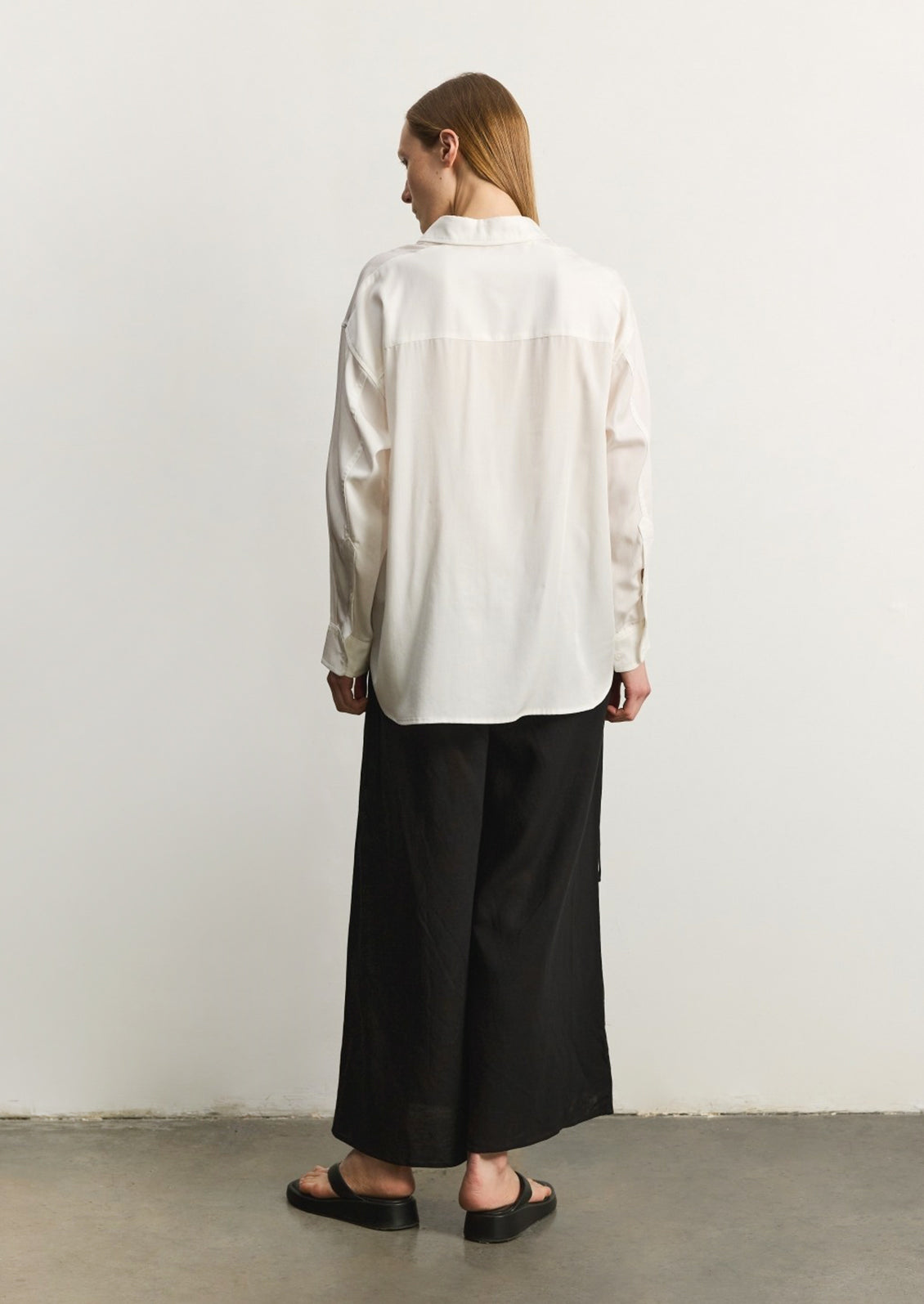 A woman wearing a relaxed, fluid fabric white button front shirt.
