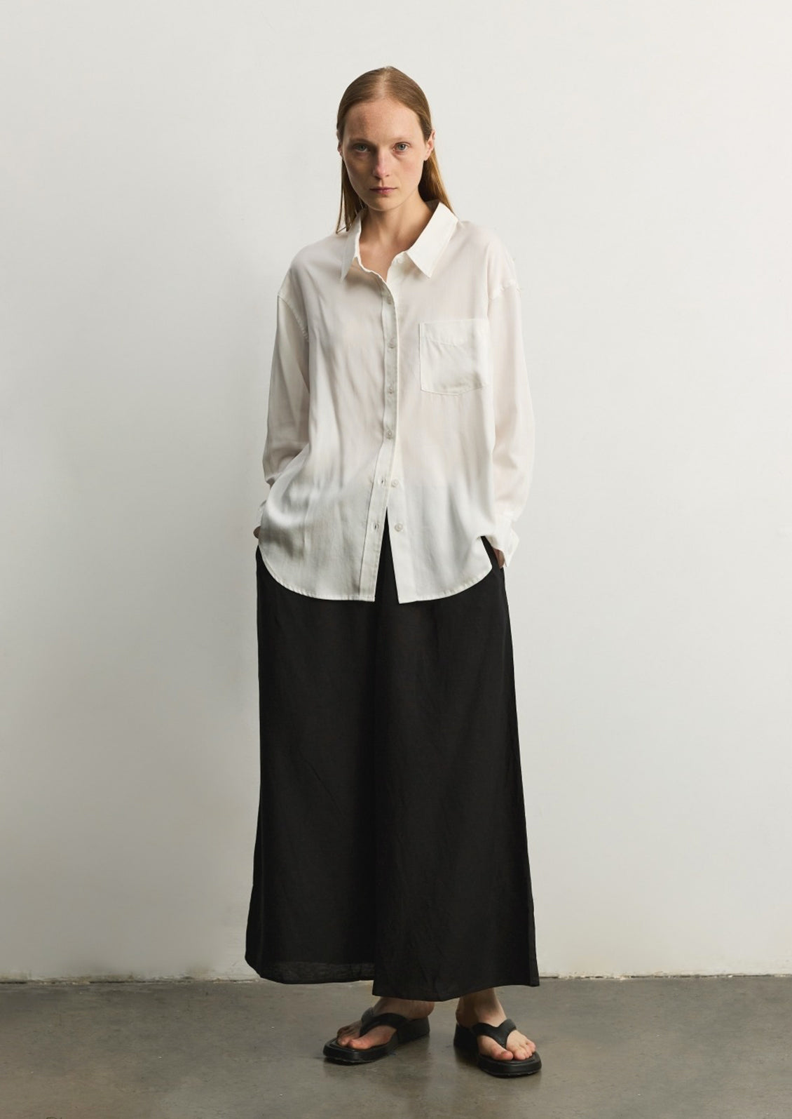 A woman wearing a relaxed, fluid fabric white button front shirt.
