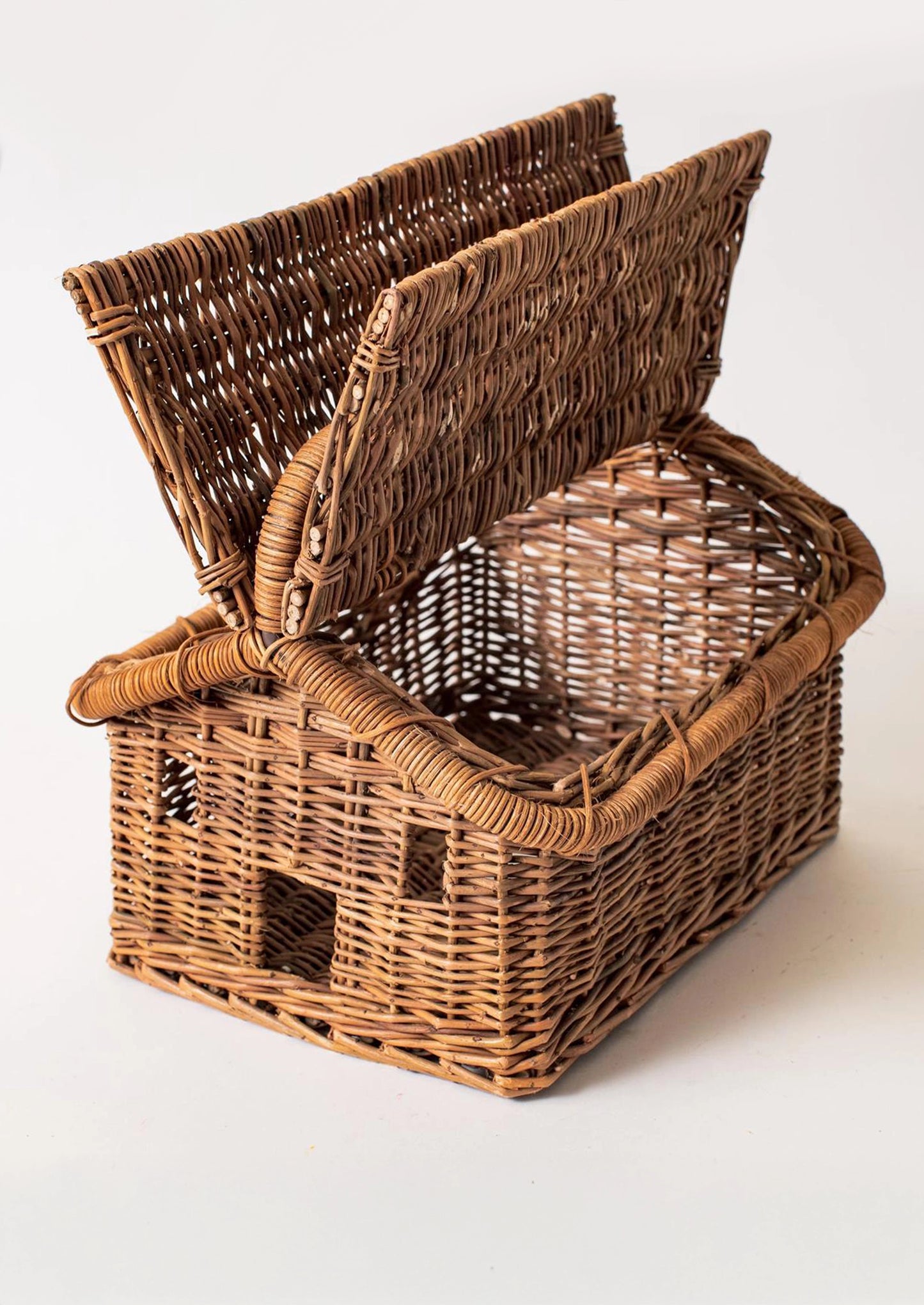 A rustic brown woven wicker basket shaped like a small house, with the lid propped open.