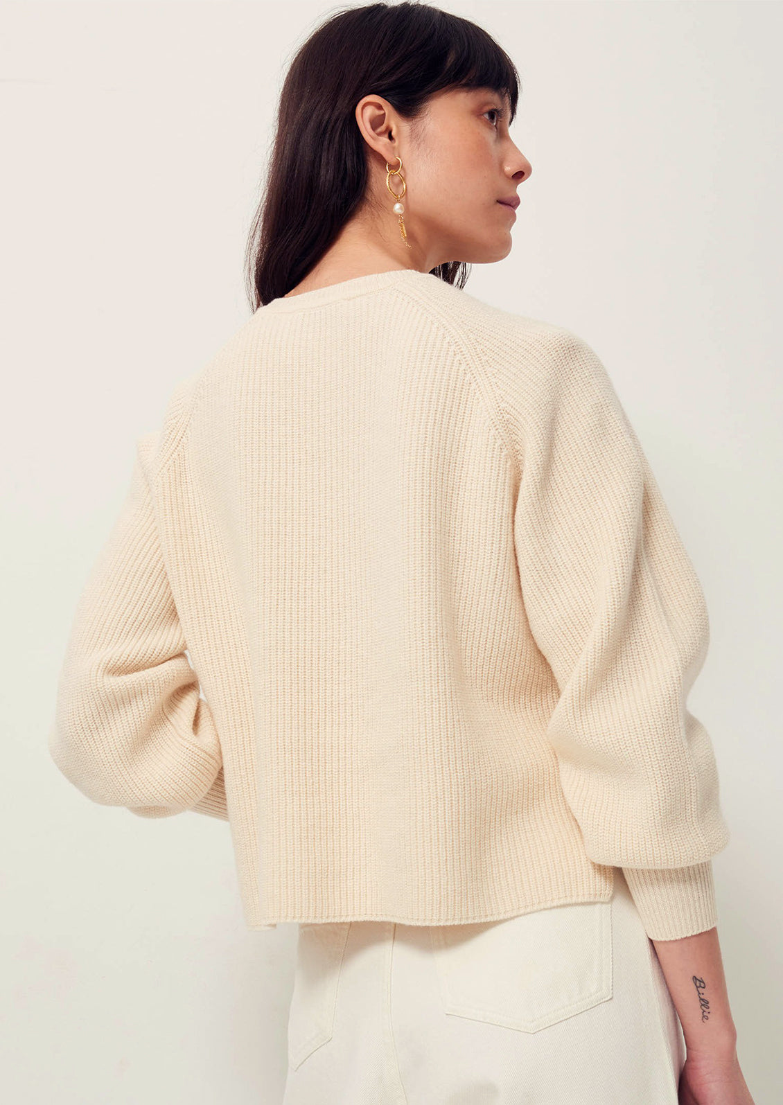 A woman wearing a cream colored sweater with cutout details and contrast tie at neck.