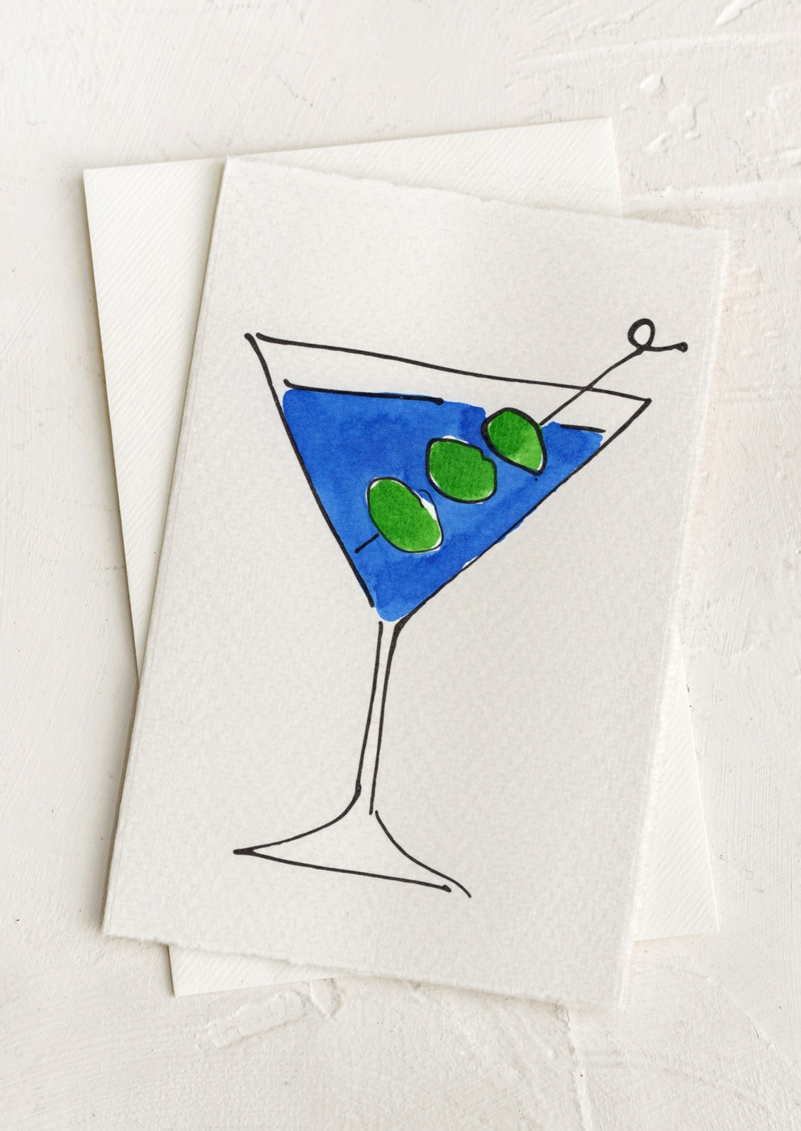 A blank greeting card with hand painted illustration of a blue martini with olives.