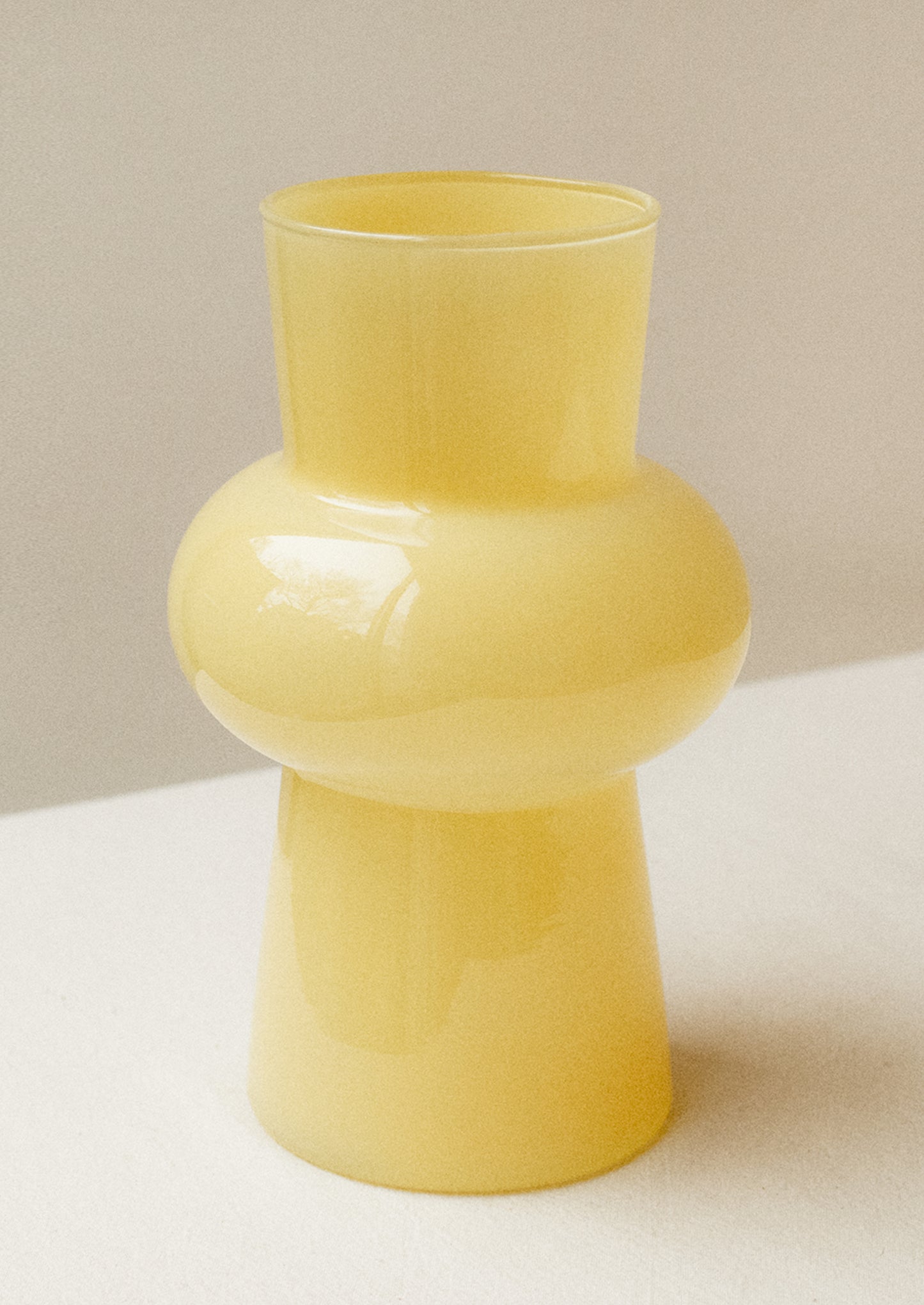 A glass vase with bulbous middle in opaque butter yellow hue.