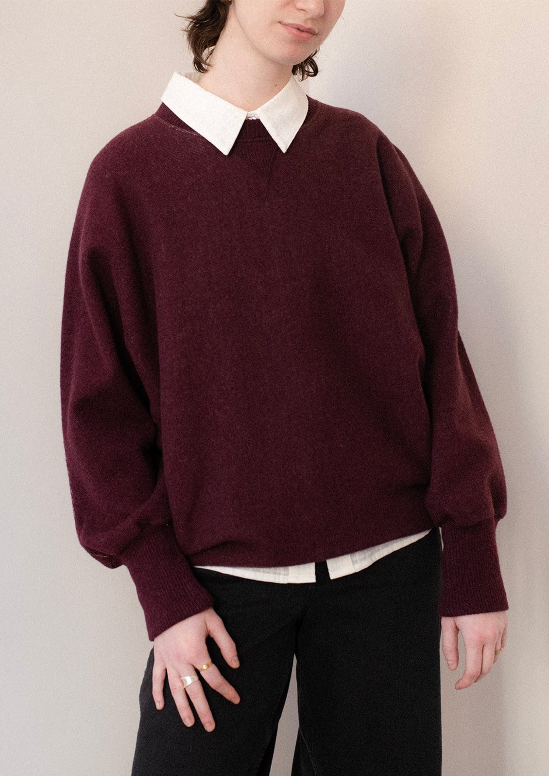 A woman wearing a sweater in burgundy with sweatshirt style silhouette.