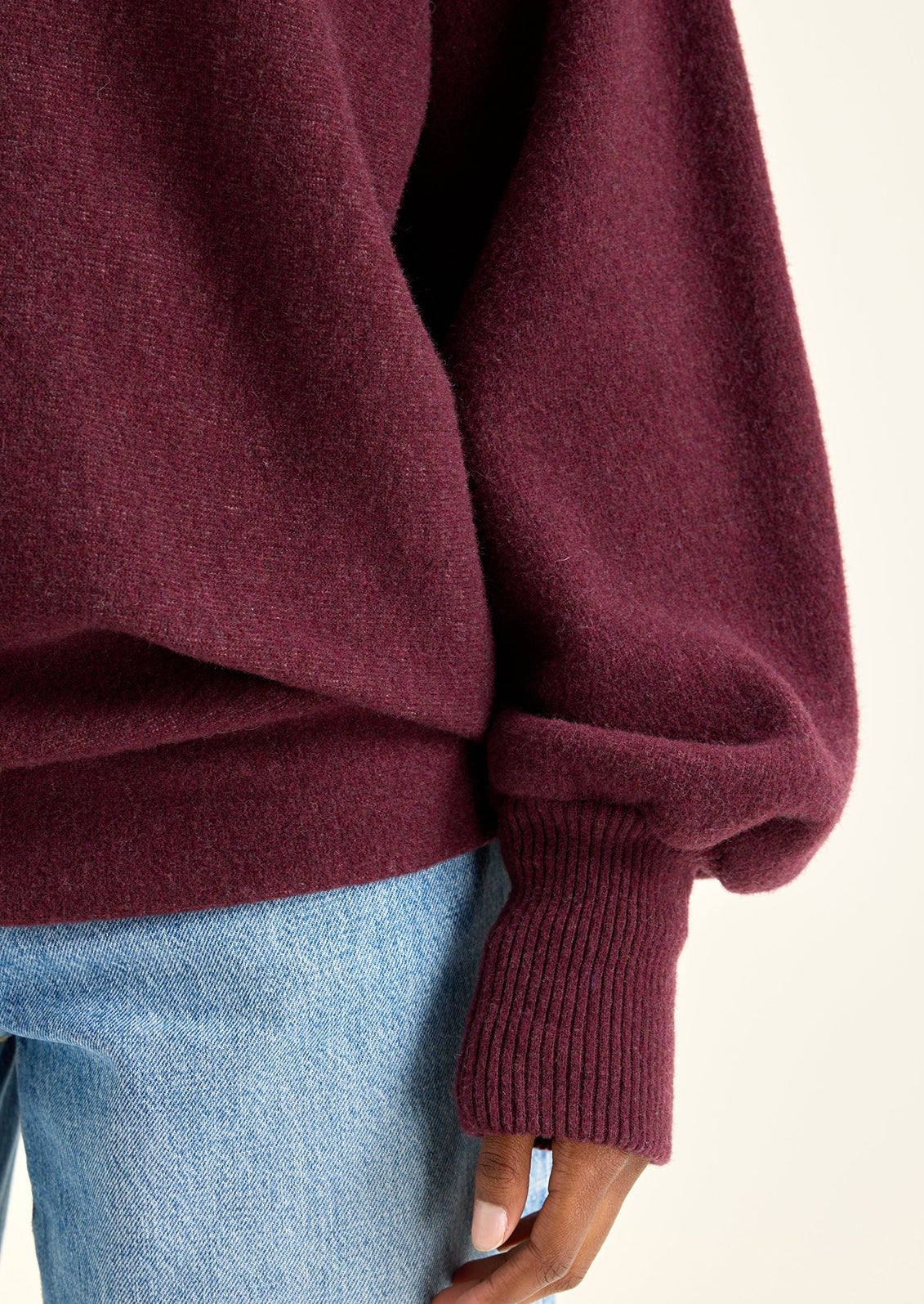 A woman wearing a sweater in burgundy with sweatshirt style silhouette.