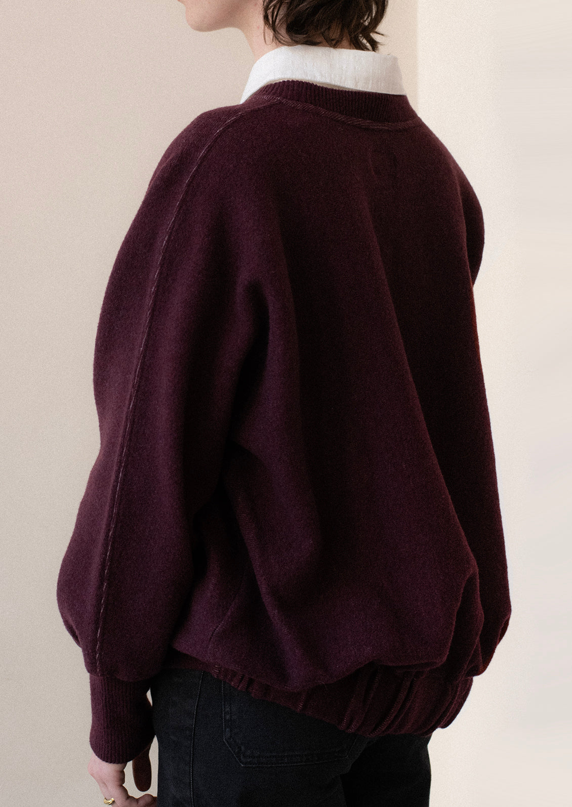 A woman wearing a sweater in burgundy with sweatshirt style silhouette.