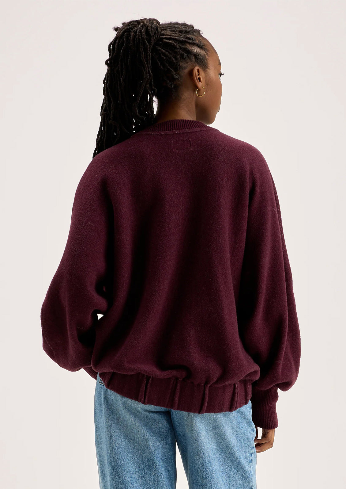 A woman wearing a sweater in burgundy with sweatshirt style silhouette.