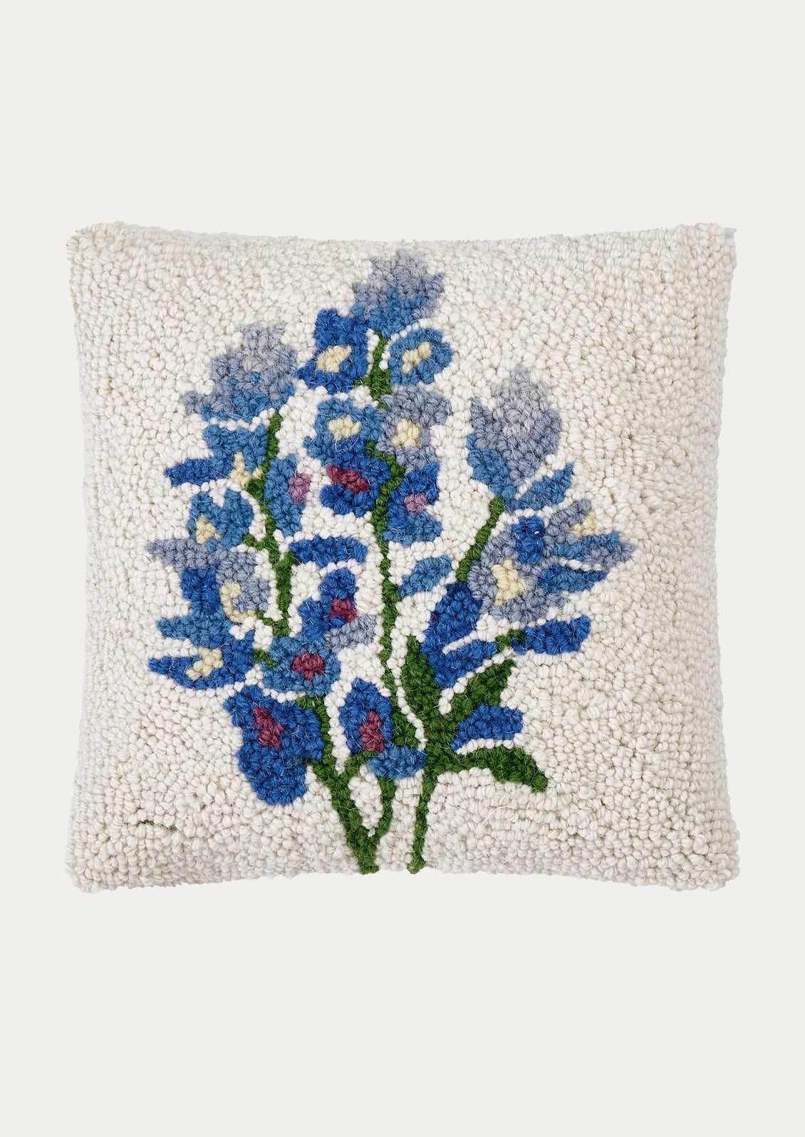 A square off-white textured throw pillow featuring a hand-hooked floral design of blue lupines with green stems and small red accents, set against a solid light gray background.