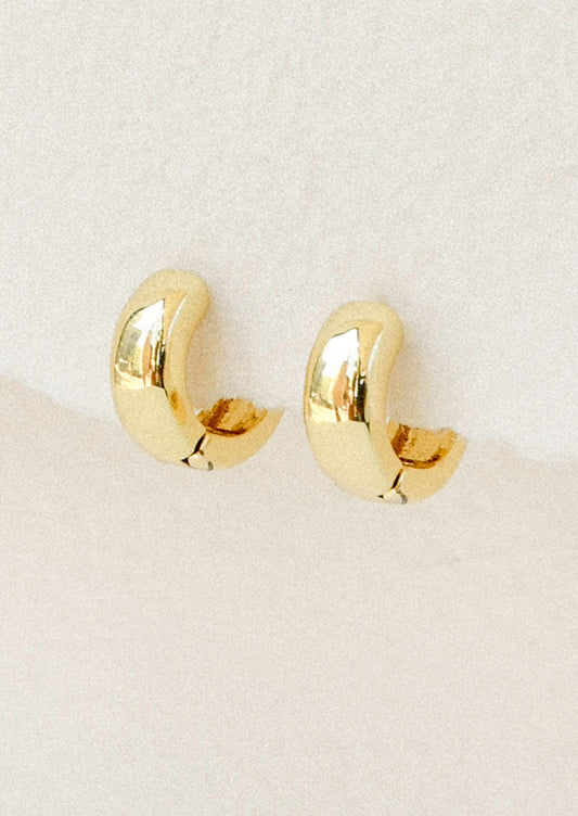 A pair of small gold huggie hoop earrings hanging from a white paper.