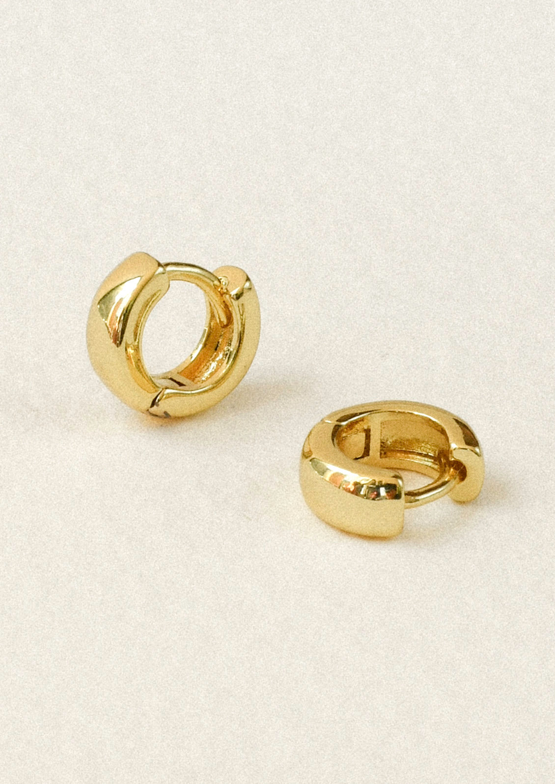 A pair of small gold huggie hoop earrings sitting on a white background.