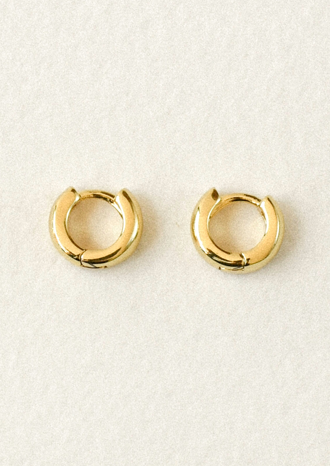 A pair of small gold huggie hoop earrings sitting on a white background.