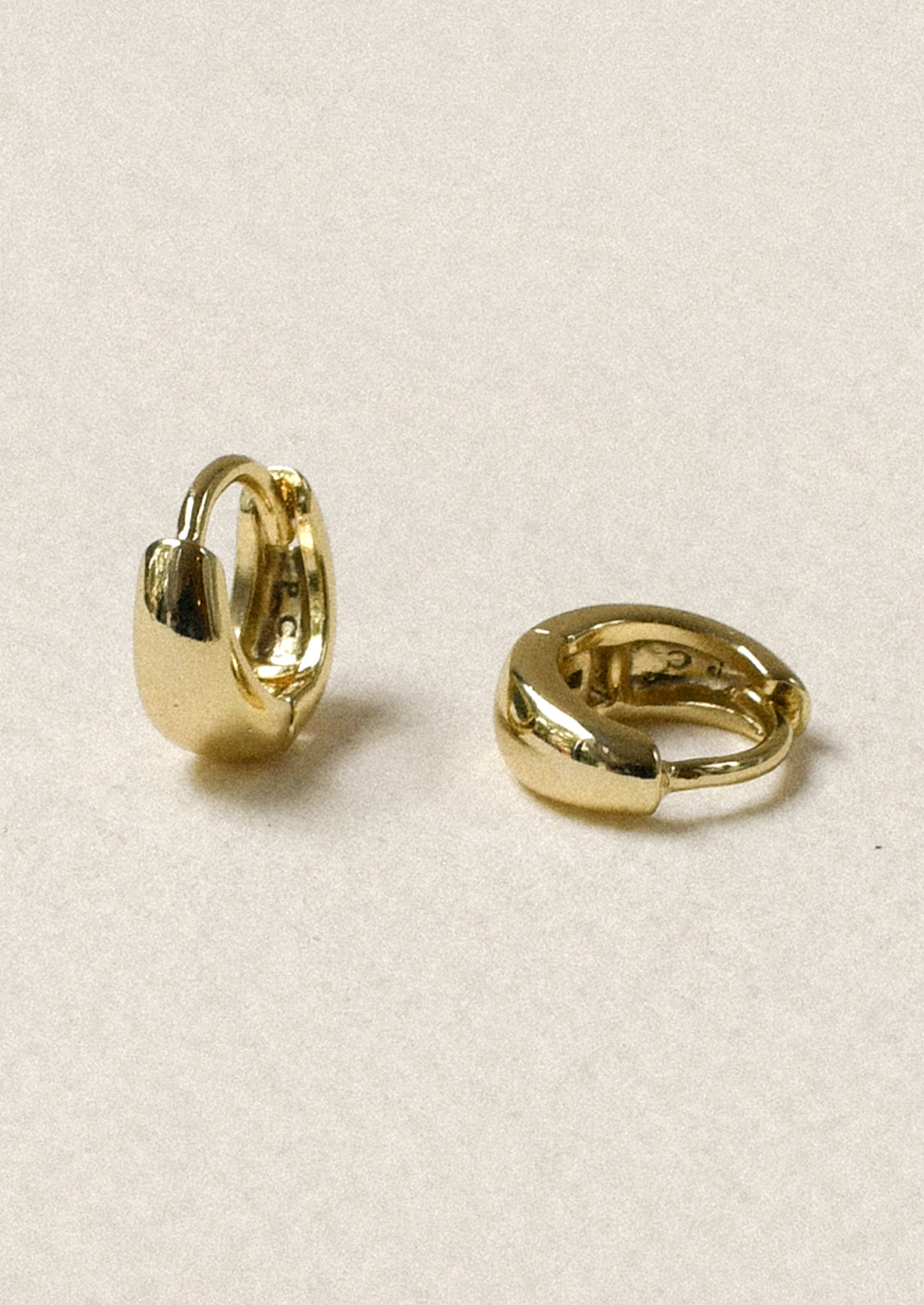 A pair of tiny gold tapered hoop earrings.