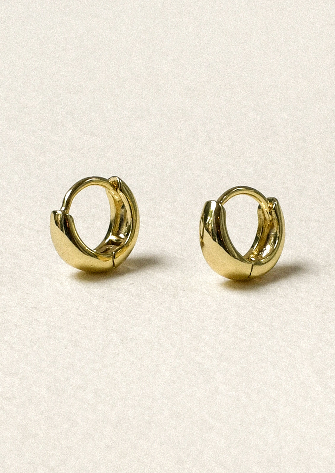 A pair of tiny gold tapered hoop earrings.