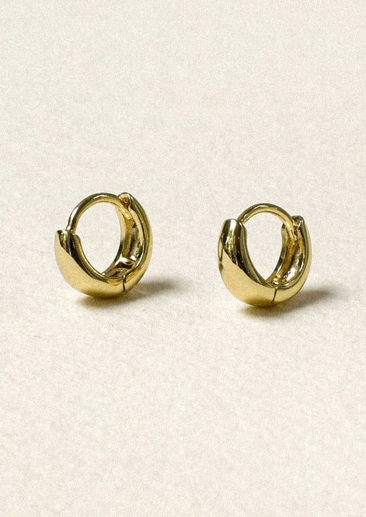 A pair of tiny gold tapered hoop earrings.