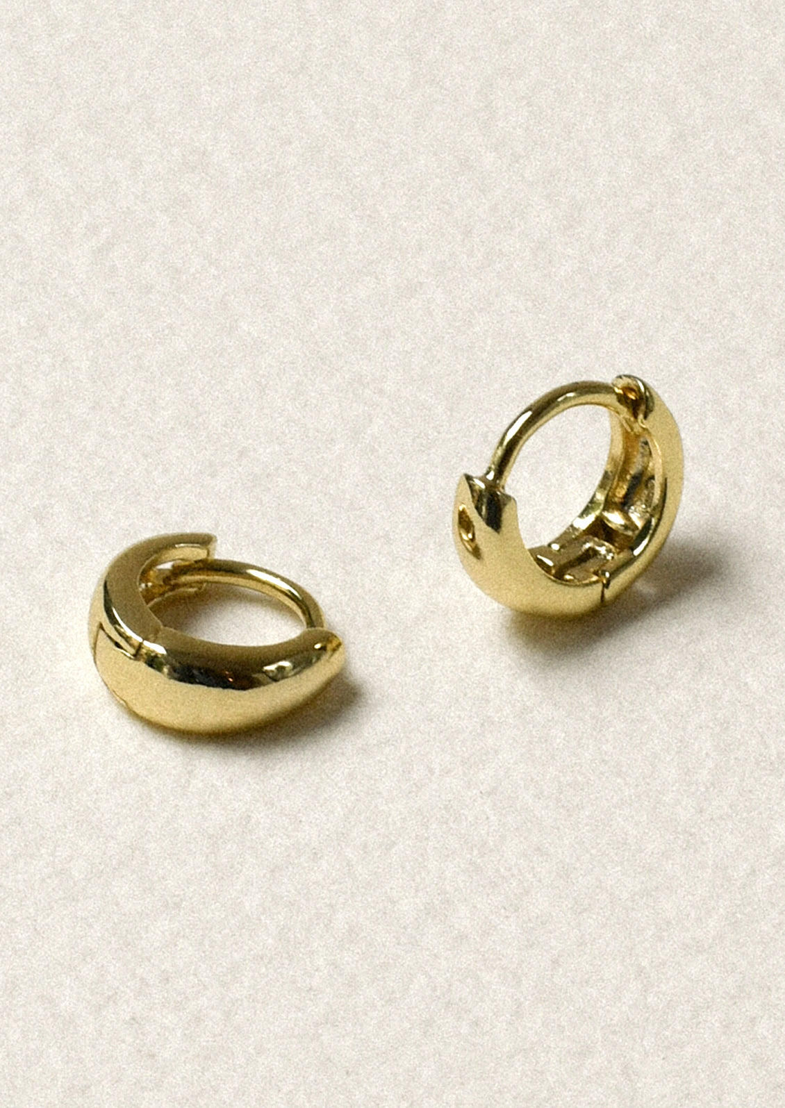 A pair of tiny gold tapered hoop earrings.