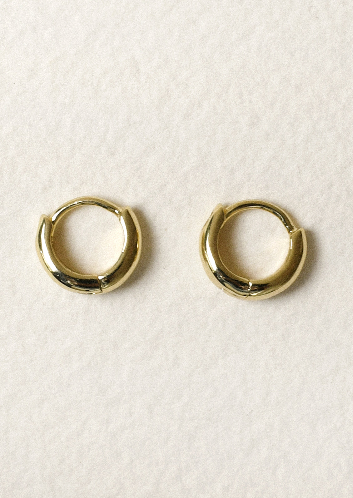 A pair of tiny gold tapered hoop earrings.