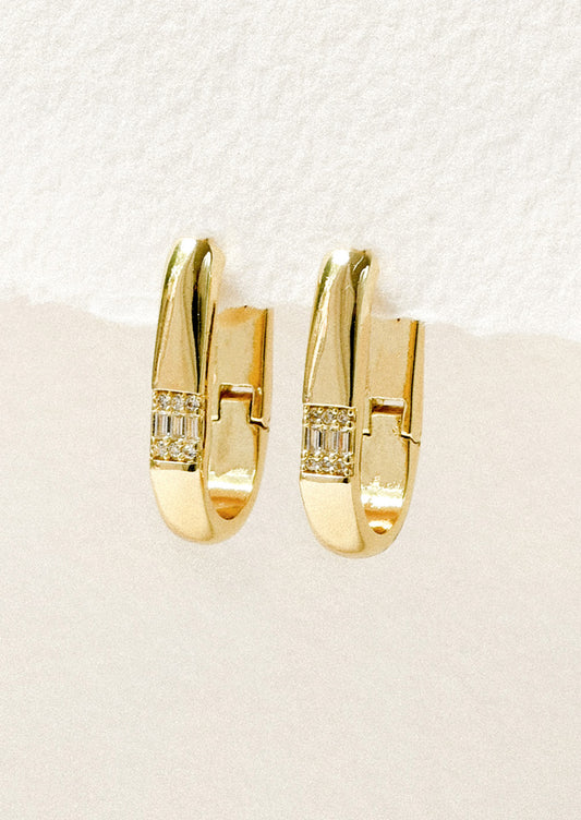 A pair of gold oval hoop earrings adorned with crystals hanging on a white background.