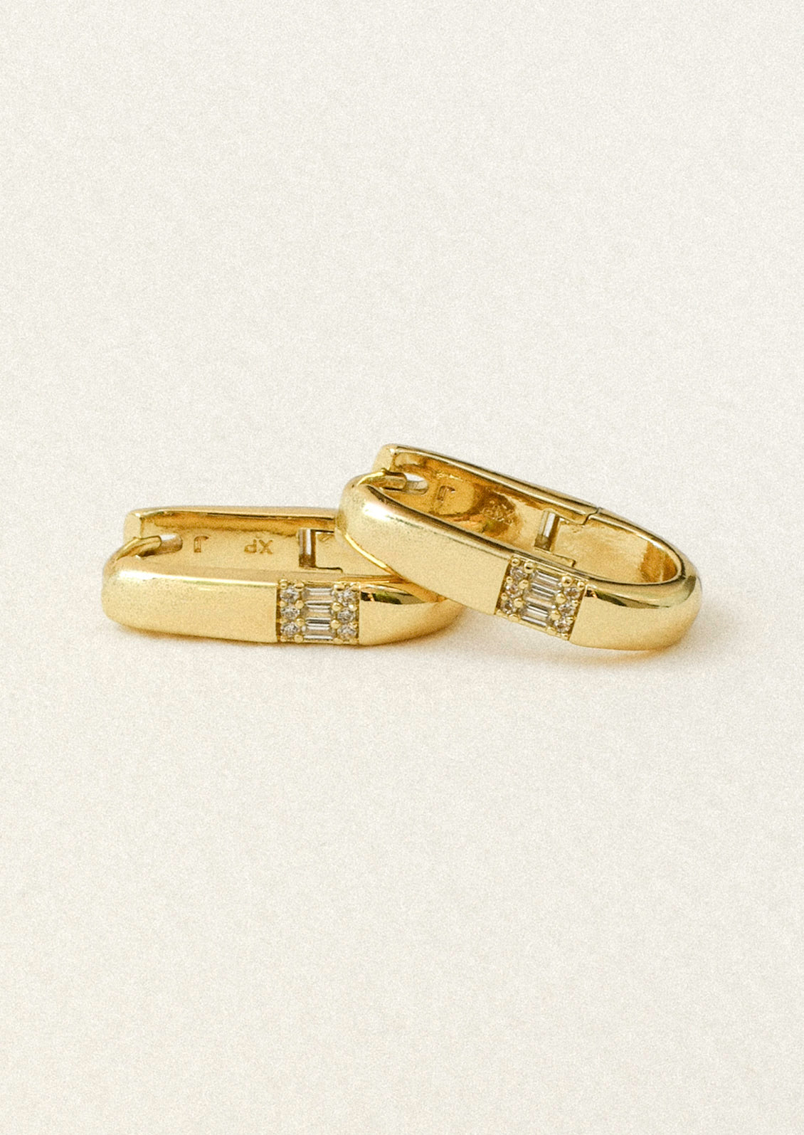 A pair of gold oval hoop earrings adorned with crystals on a white background.