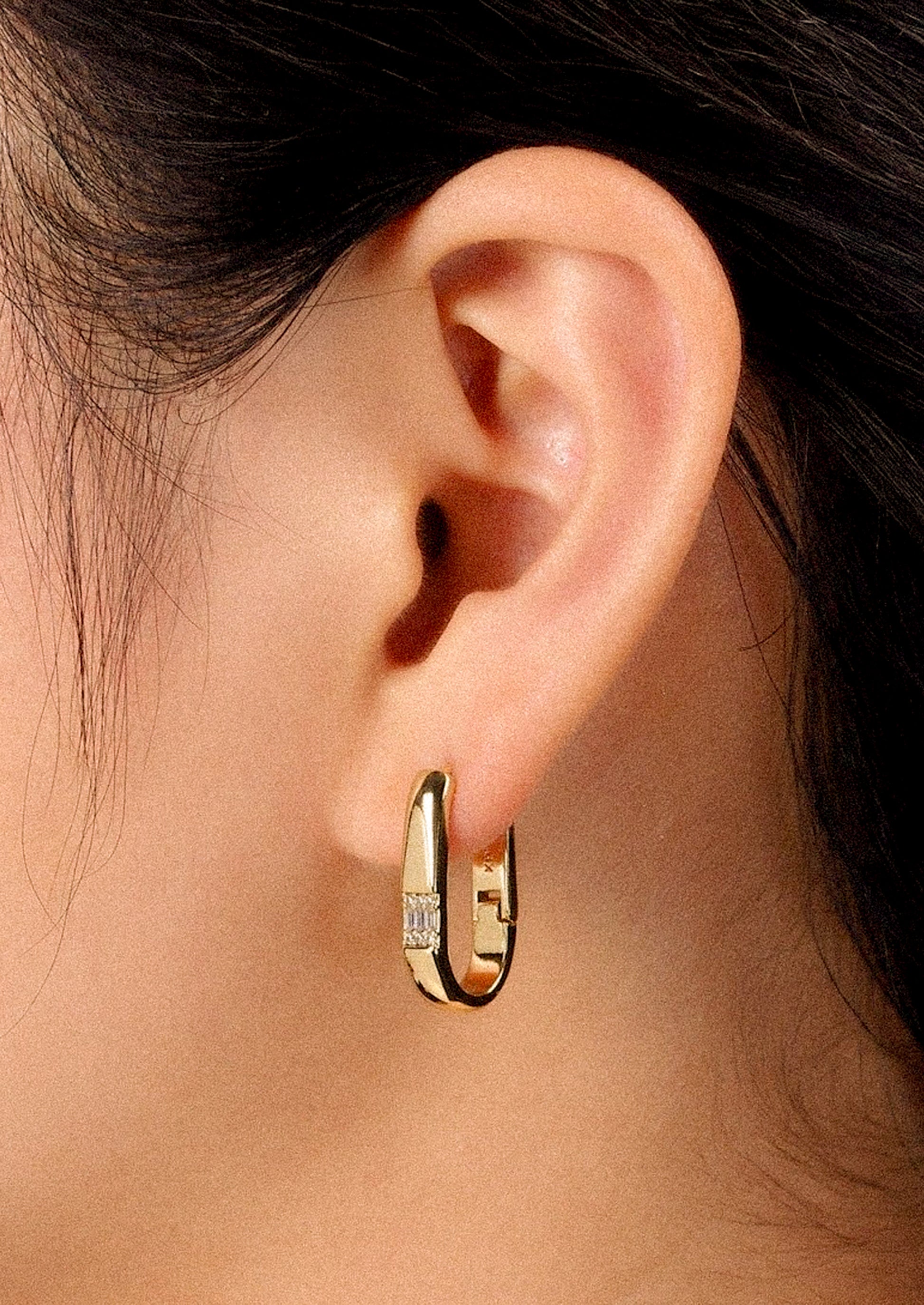 A woman wearing a gold oval-shaped earring with crystals.